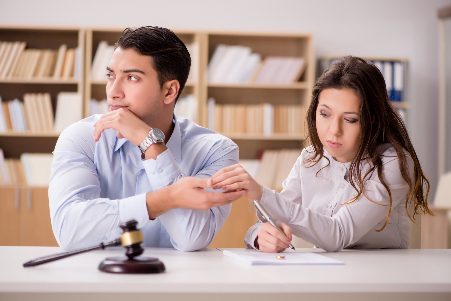 Two people in an office signing papers beside a judge’s gavel, one looking thoughtful and one writing.