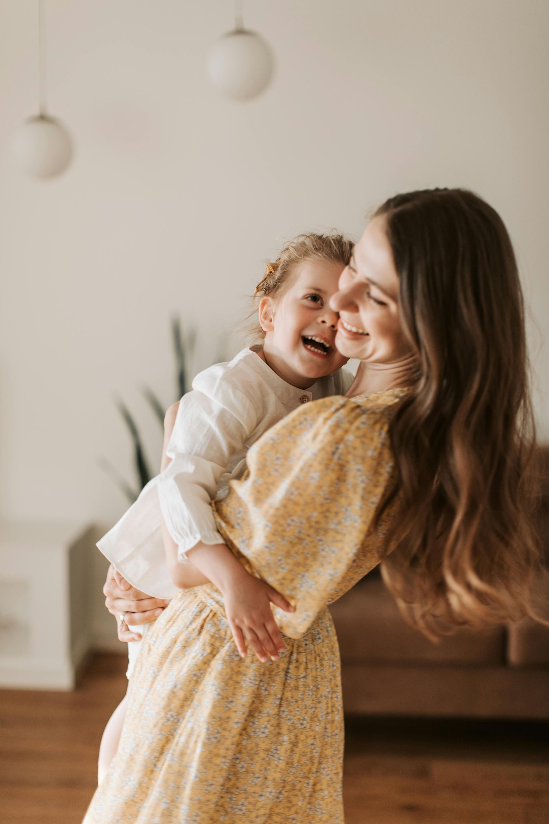 Smiling woman holding a laughing child in a warm, sunlit living room