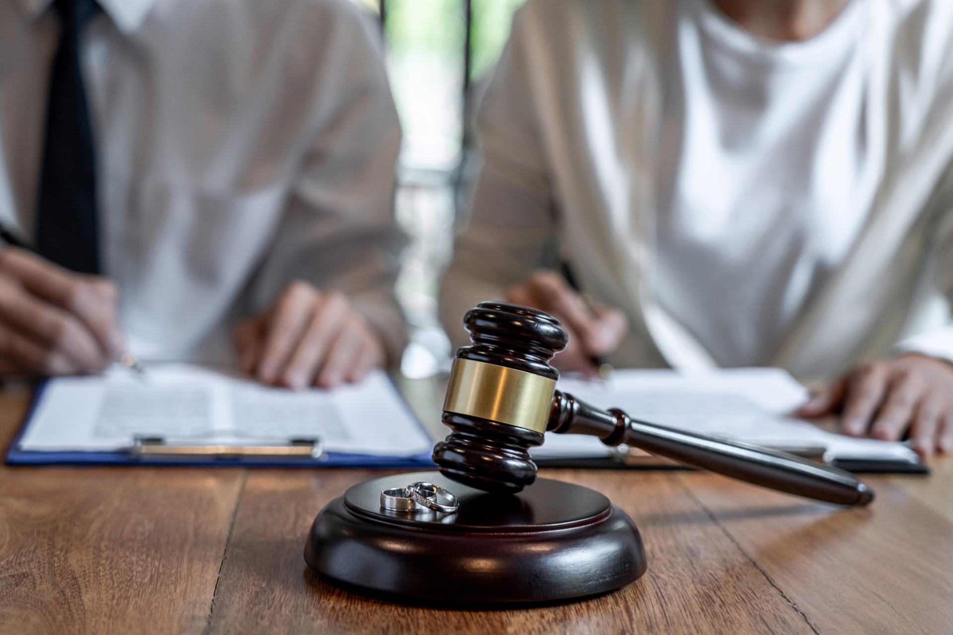 Judge's gavel on a desk with two people signing documents in the background