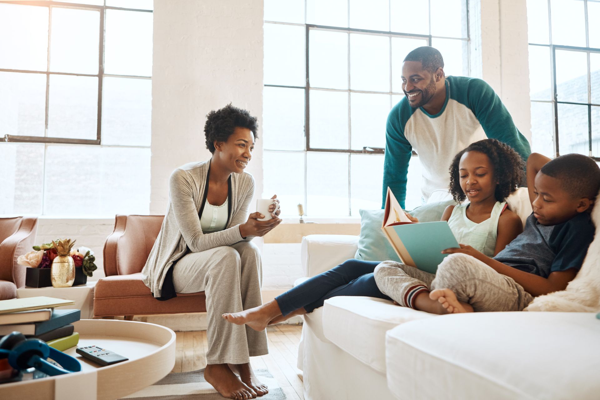 Family relaxing together on a couch in a bright living room, smiling and reading a book