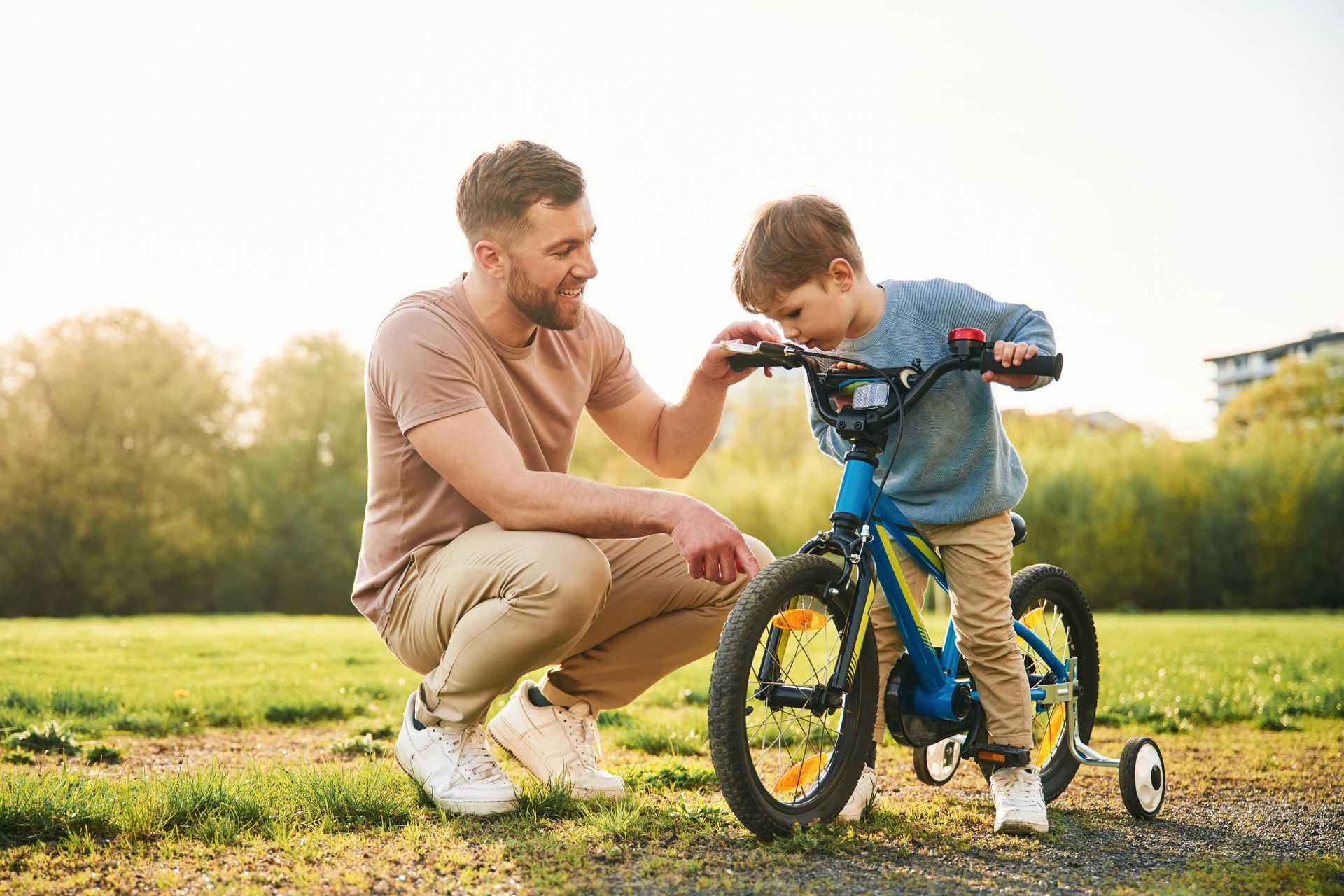 Man helping child ride a blue bicycle on grass in a sunny park