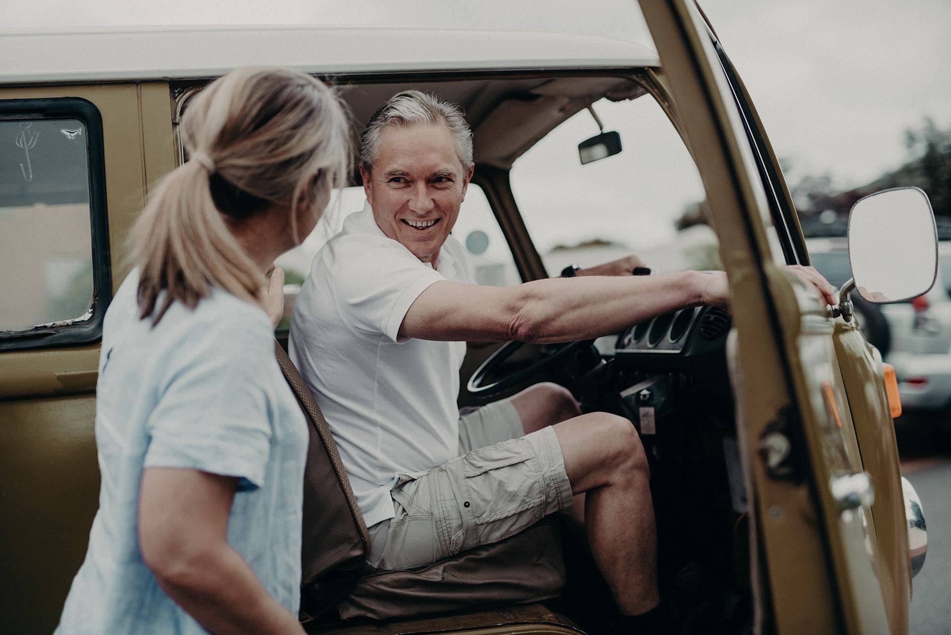A man is sitting in the driver 's seat of a van while a woman stands next to him.