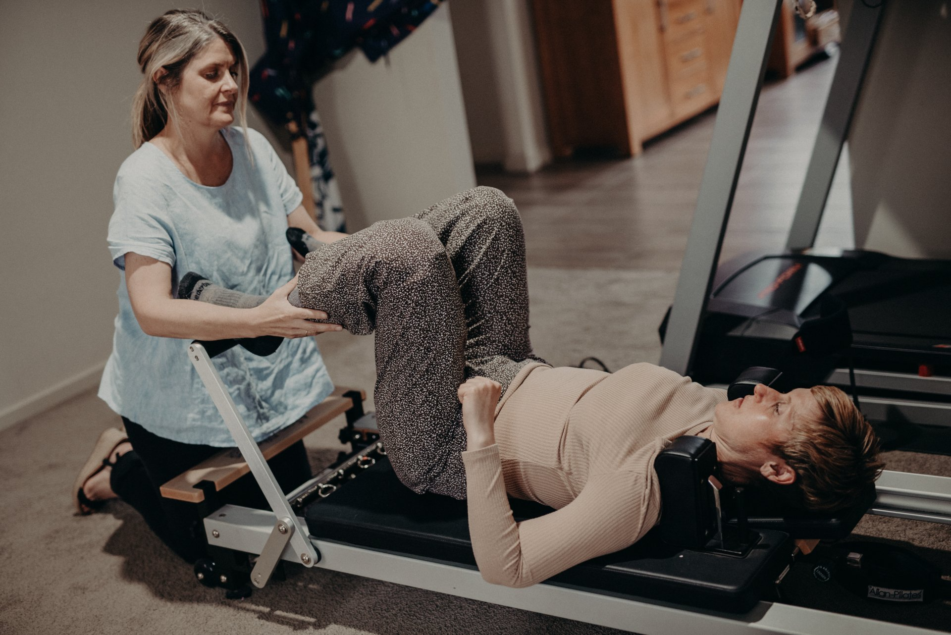 A woman is helping a woman do exercises on a machine.