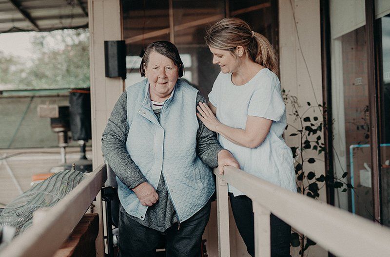 A woman is helping an elderly woman walk down a ramp.
