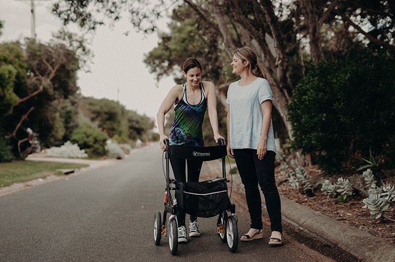 Two women are walking down a street with a walker.