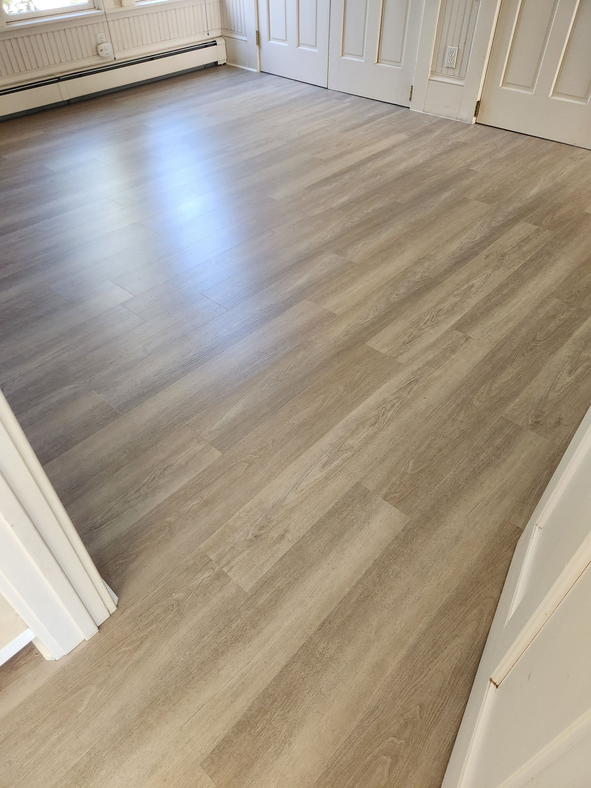 Empty room with light wood flooring and white walls near a doorway and radiator.