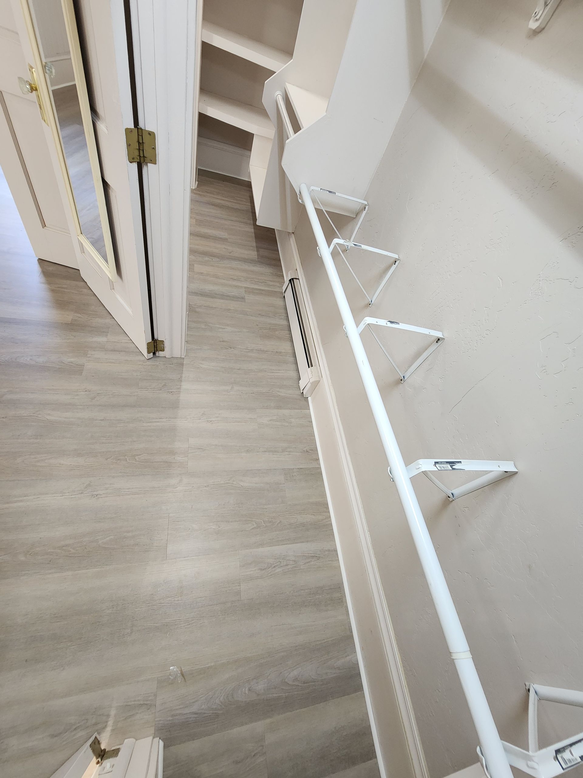 Indoor staircase with light wood flooring and white handrails in a narrow hallway.