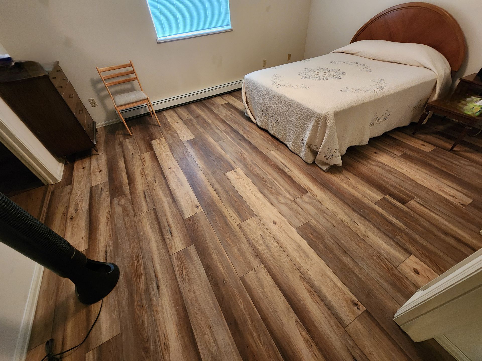 Empty bedroom with wooden floor, single bed, small window, and radiator by the wall.