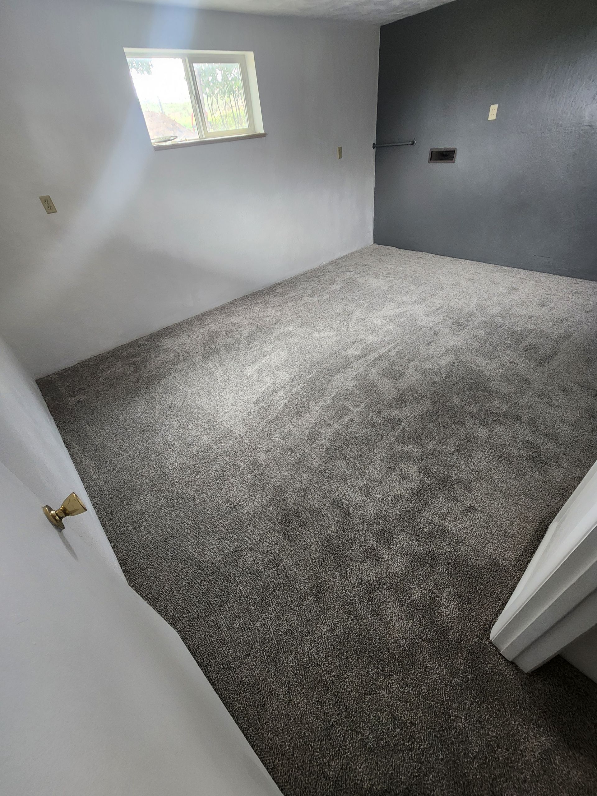 Empty bedroom with gray walls, carpeted floor, and a small window.