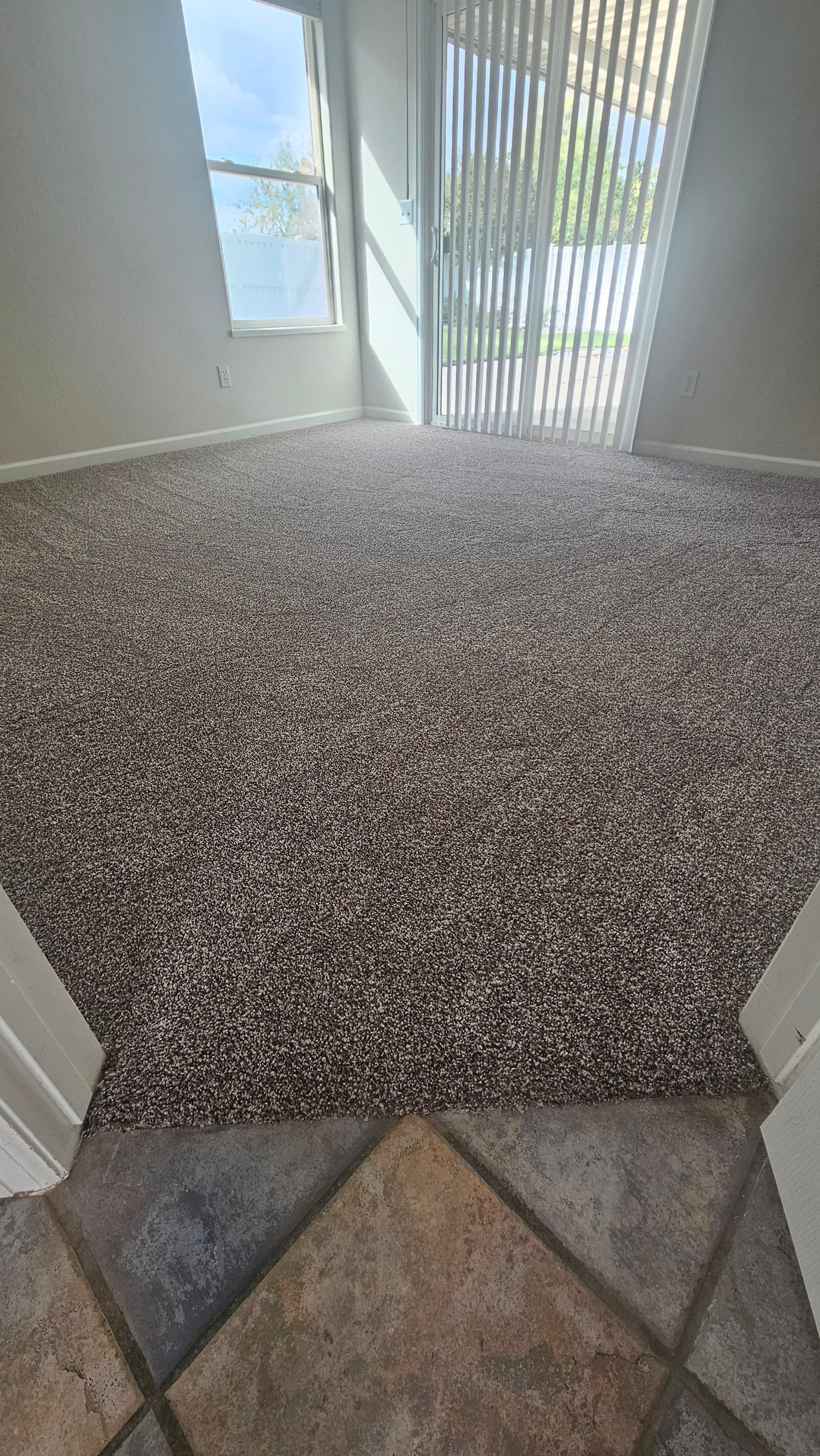 Entryway with tile floor transitioning to carpeted stairs and a bright doorway with vertical blinds