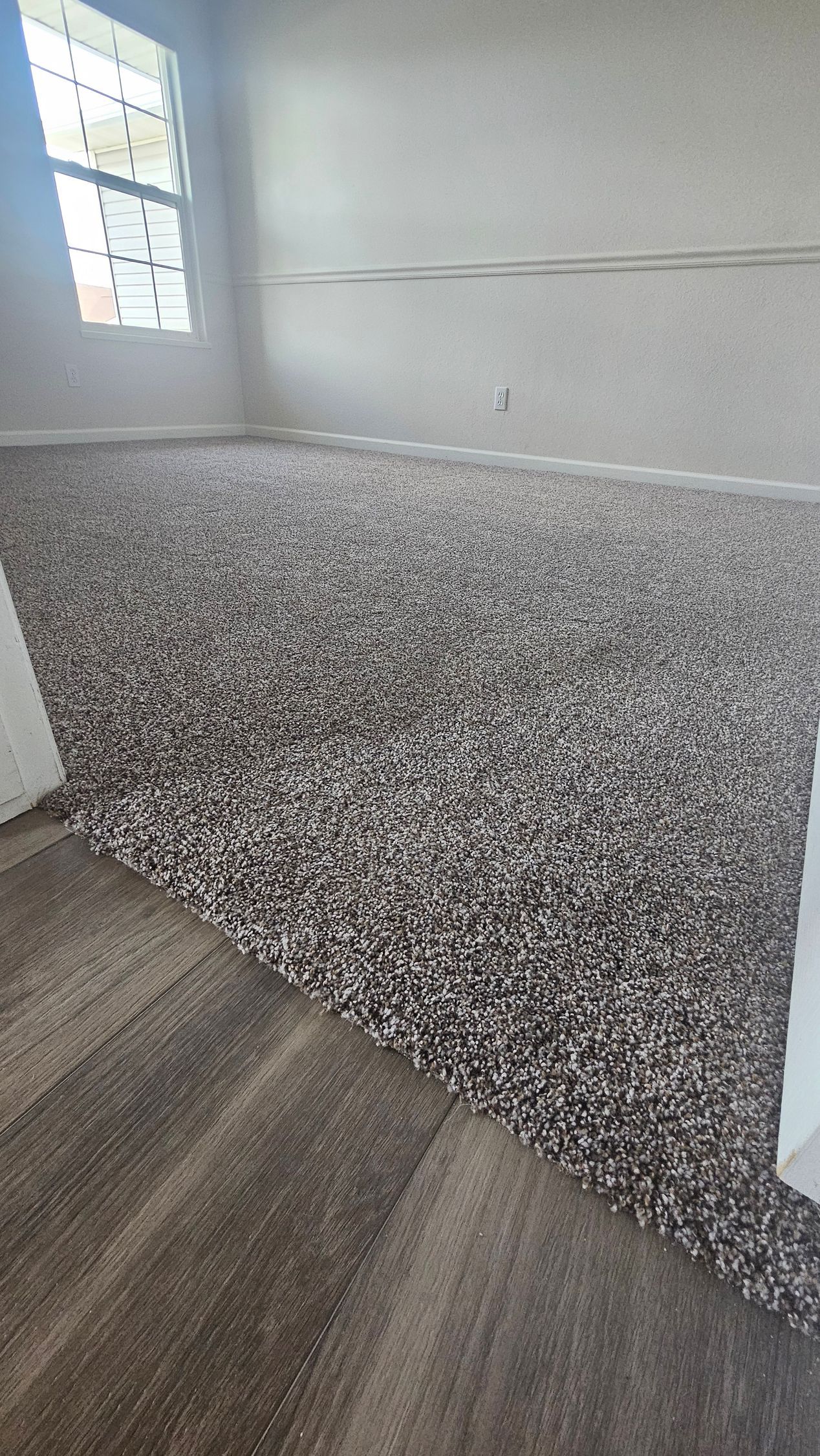 Empty room with a gray-speckled half wall, white upper walls, and a wood-look floor.