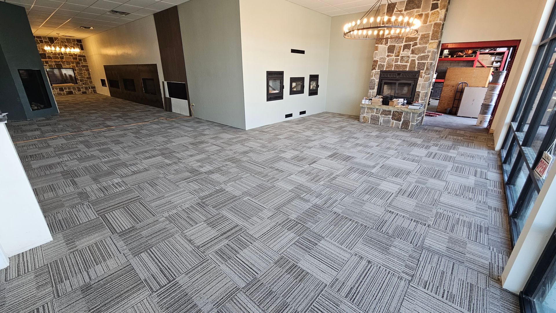 Empty modern lobby with patterned carpet, chandeliers, and seating area by large windows