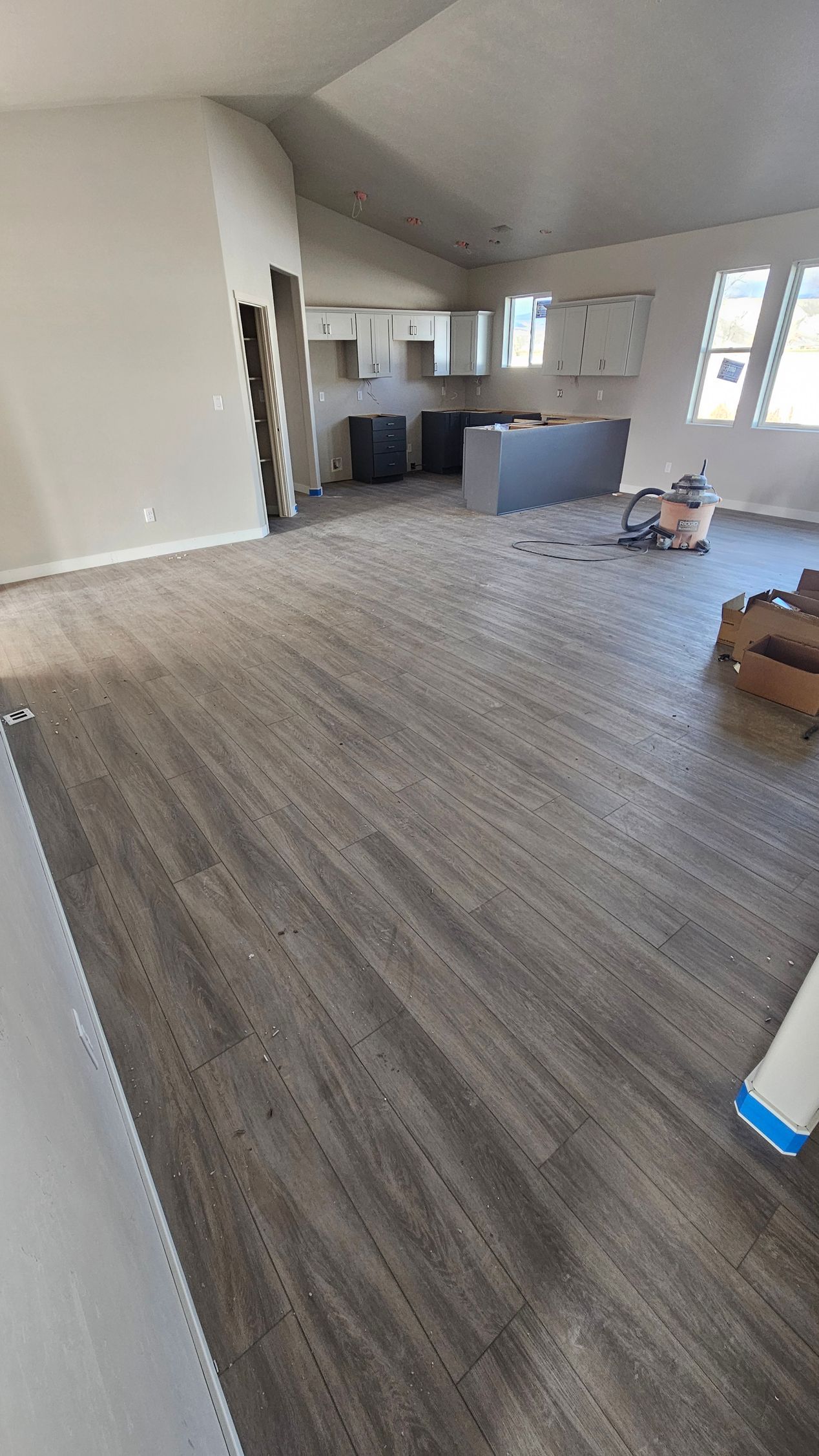 Empty open-plan kitchen and living room with gray wood floors and white walls, partially furnished.