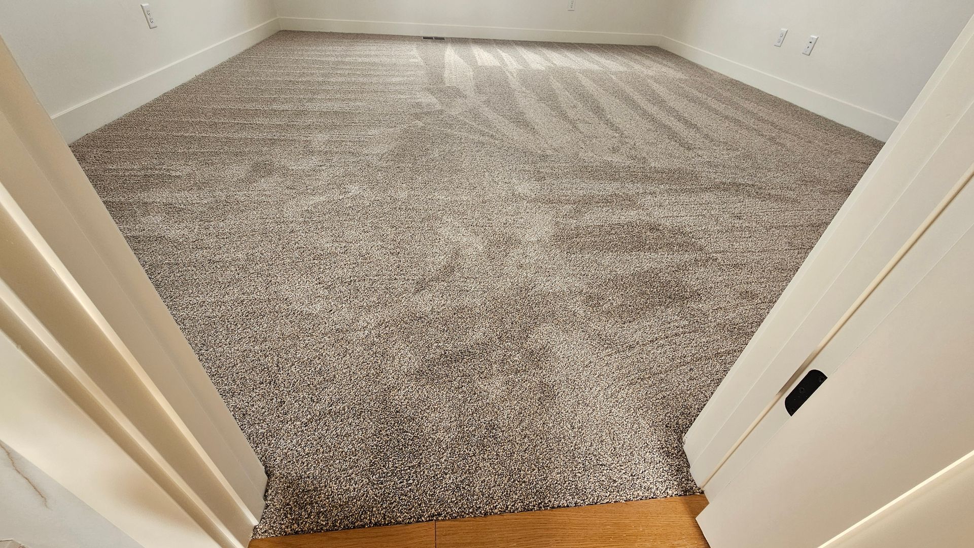 Empty carpeted room with beige walls and white trim, viewed through an open doorway