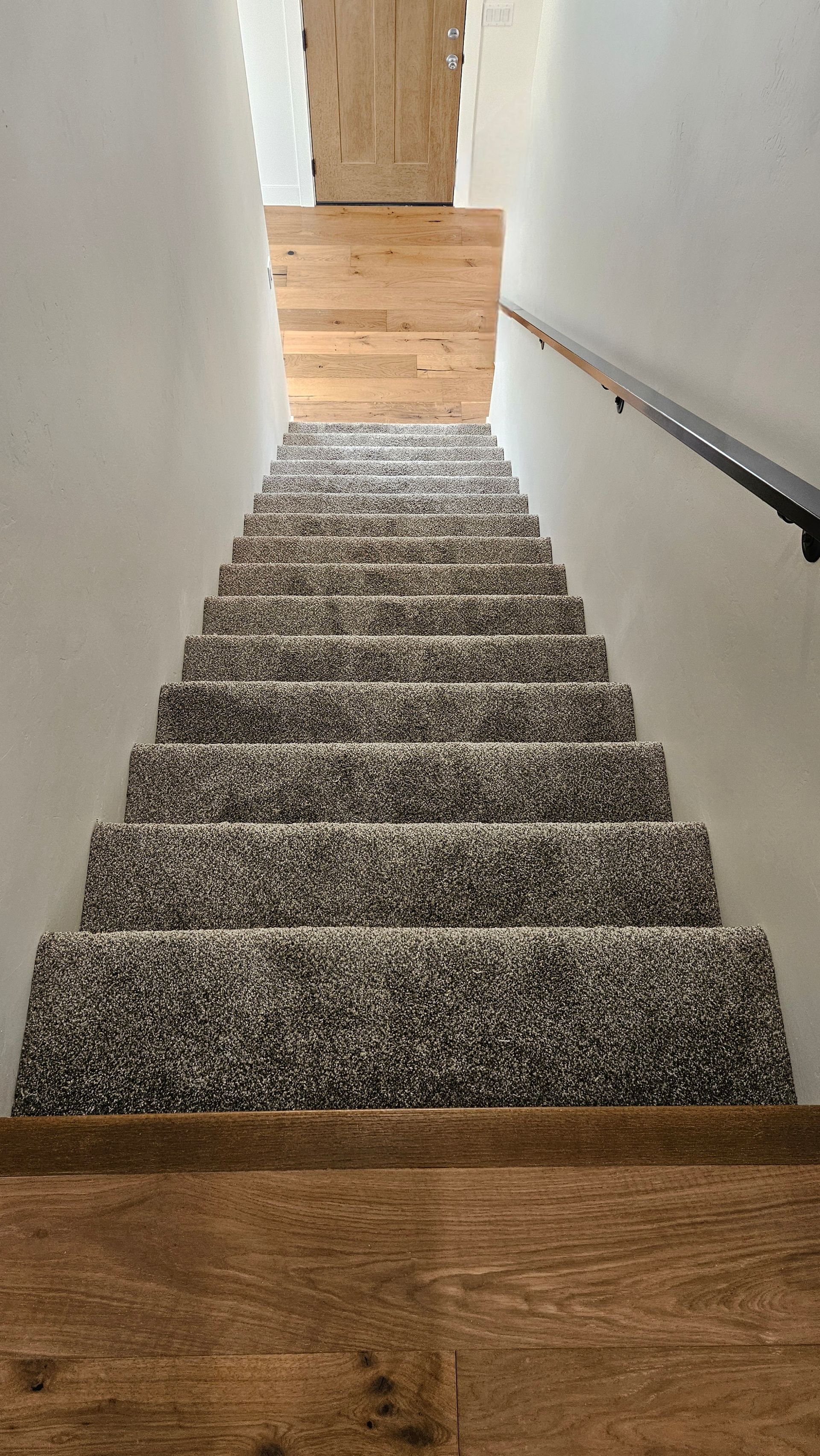 Carpeted staircase in a narrow hallway with white walls, wood trim, and a handrail on the right.