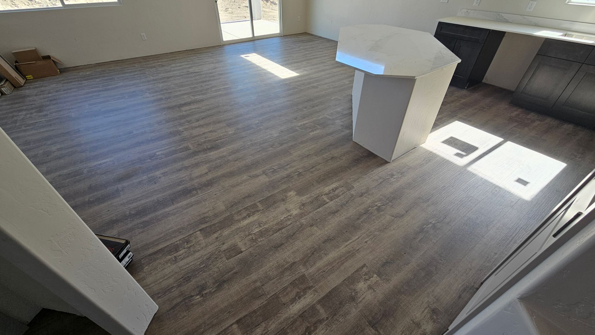 Empty room with wood-look flooring, a white table, and sunlight streaming through windows.