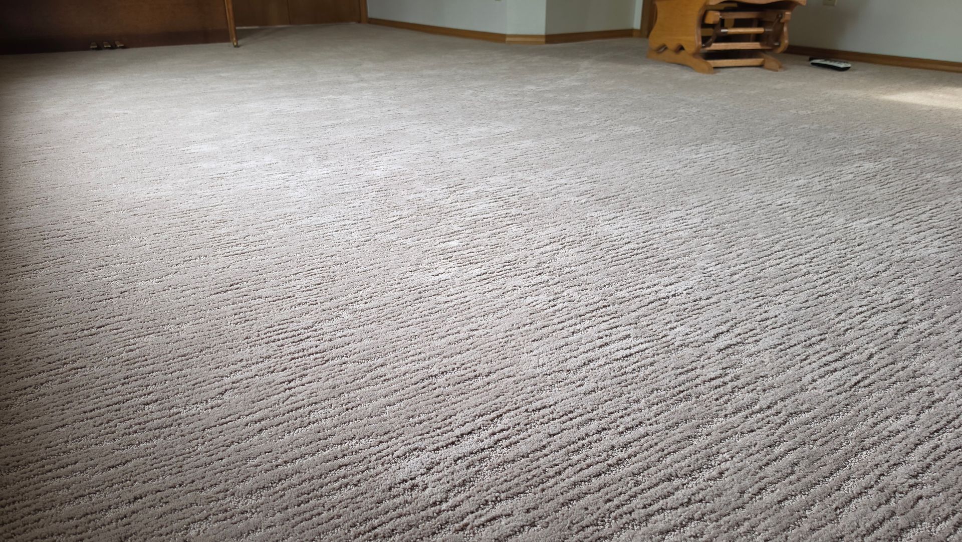 Empty beige carpeted room with a hardwood floor edge and stacked boxes in the corner