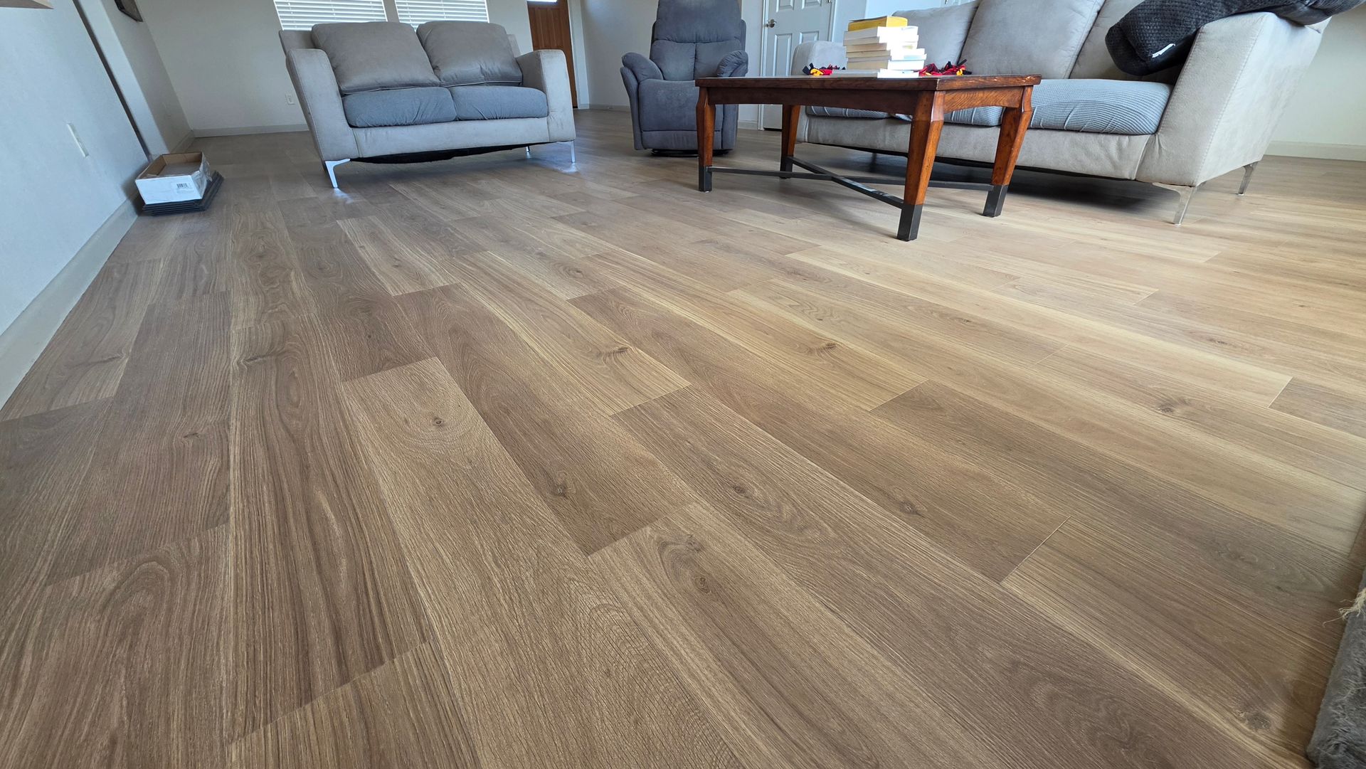 Spacious living room with wood-patterned flooring, gray sofas, and a wooden coffee table.