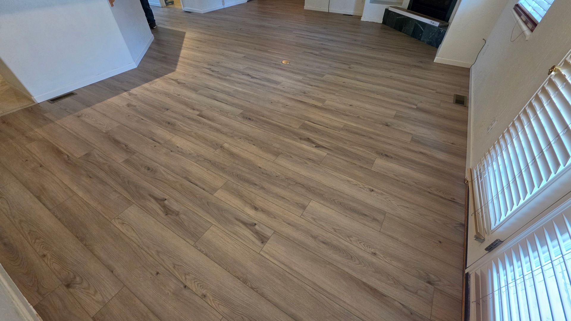 Empty room with light wood flooring and white walls, viewed from a corner near a window.
