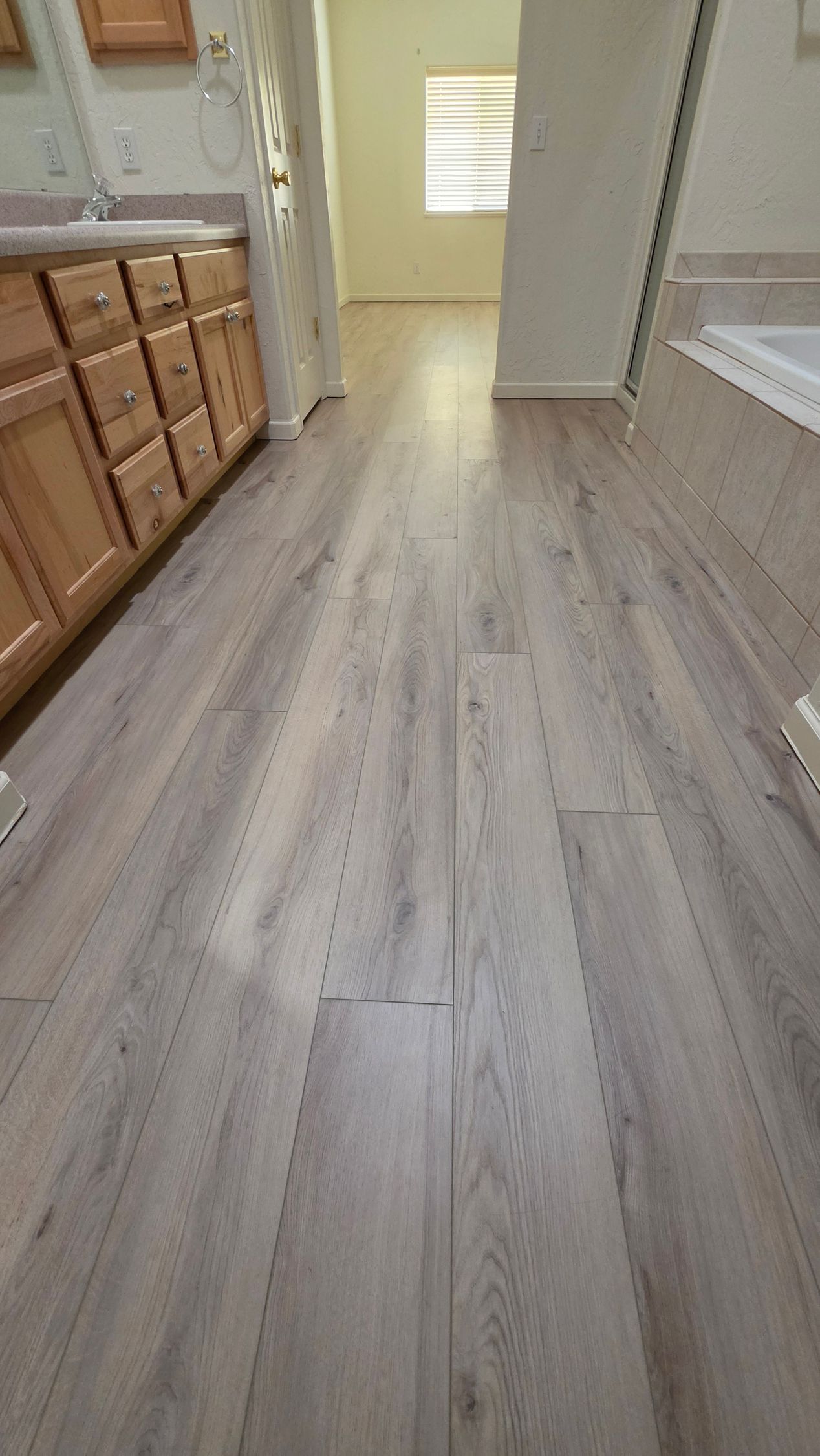 Empty hallway with light wood flooring, beige walls, and kitchen cabinets on the left.