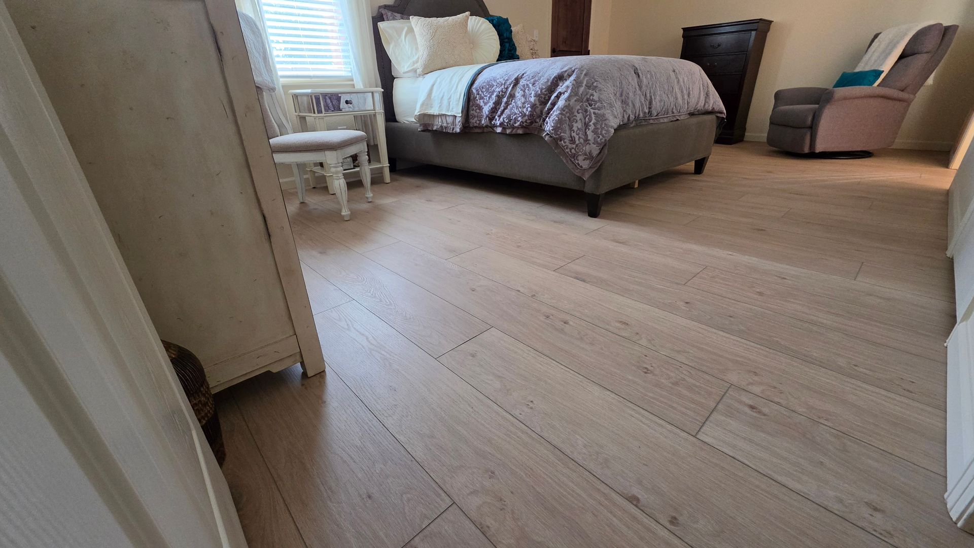Spacious bedroom with a bed, window seat, dresser, and light wood flooring.