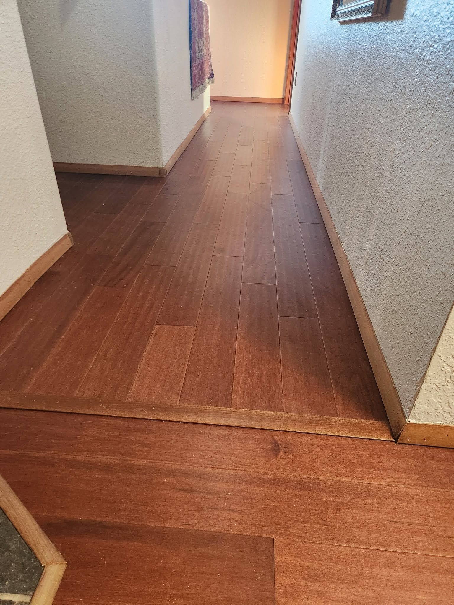 Empty hallway with wooden floor and white walls, lit by a doorway at the end.