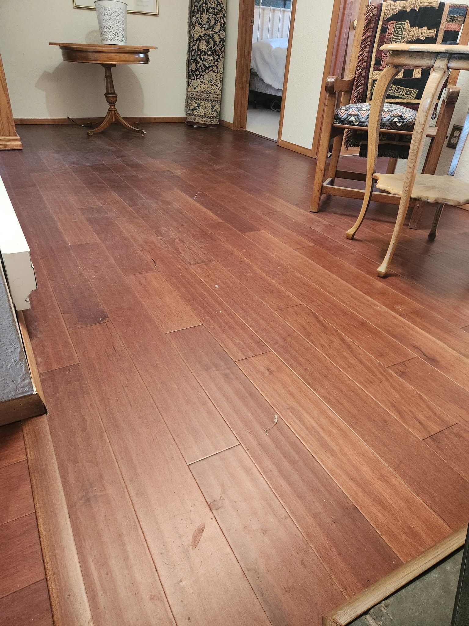 Wooden floor in a dining room with a small table, chairs, and patterned curtains.