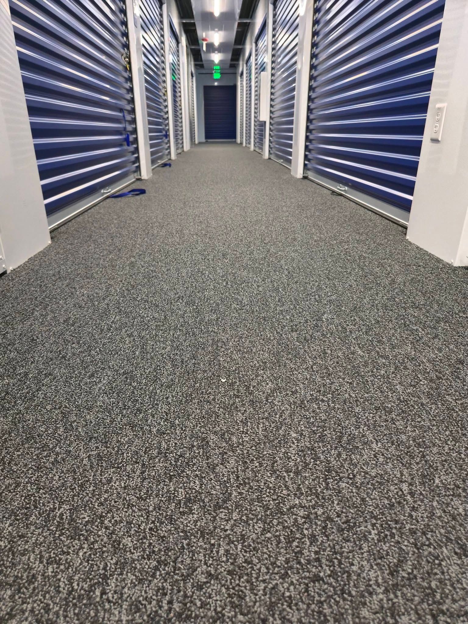 Storage facility hallway with blue roll-up doors and speckled gray carpet.