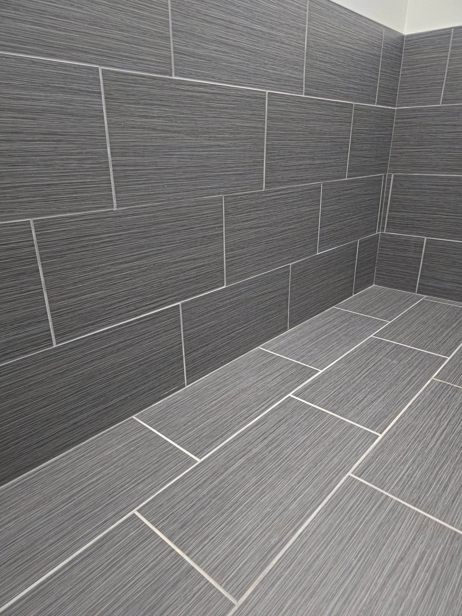 Gray tiled corner of an empty shower or bathroom wall and floor.