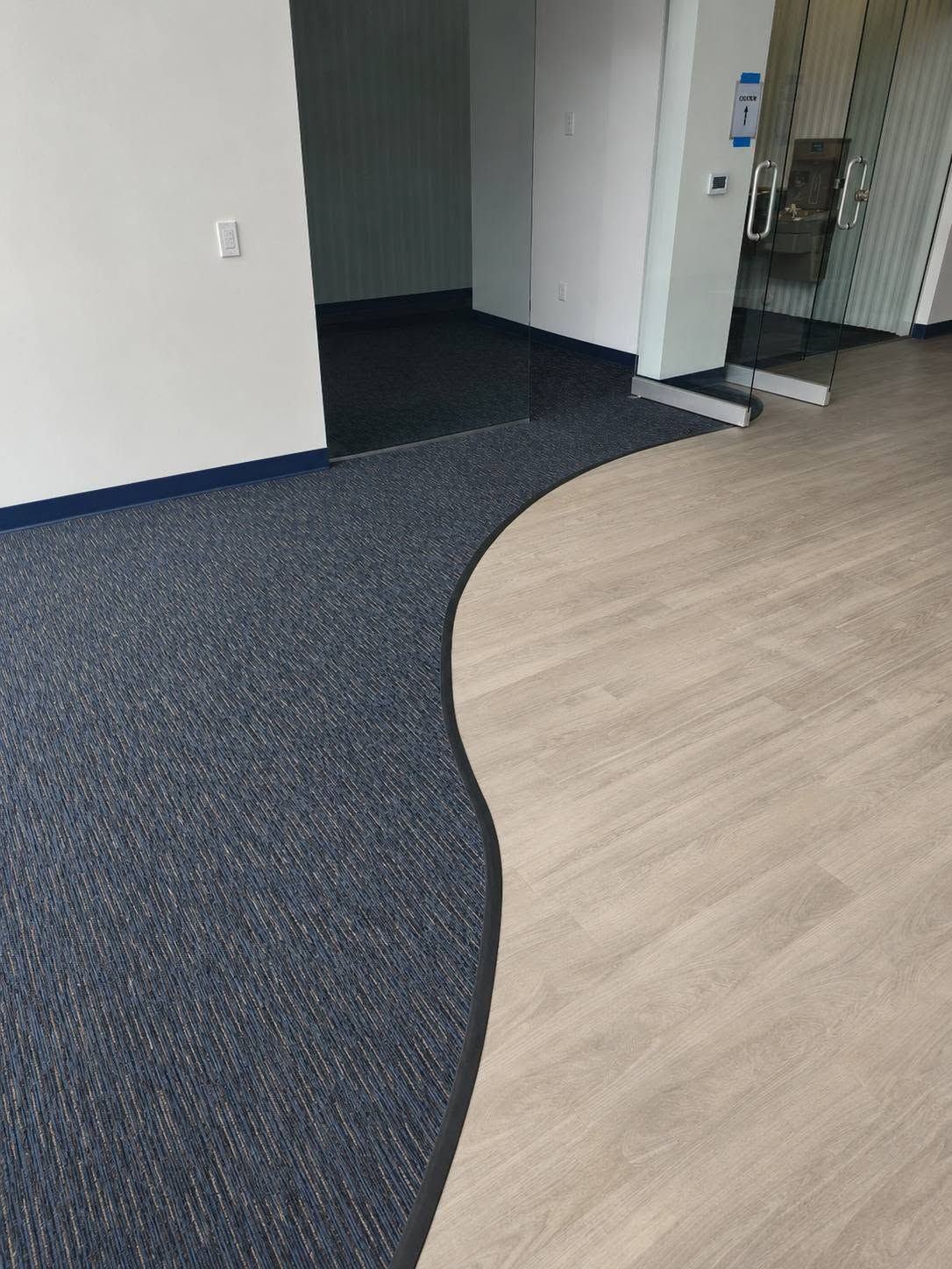 Office hallway with dark carpet and light wood flooring, separated by a curved edge.