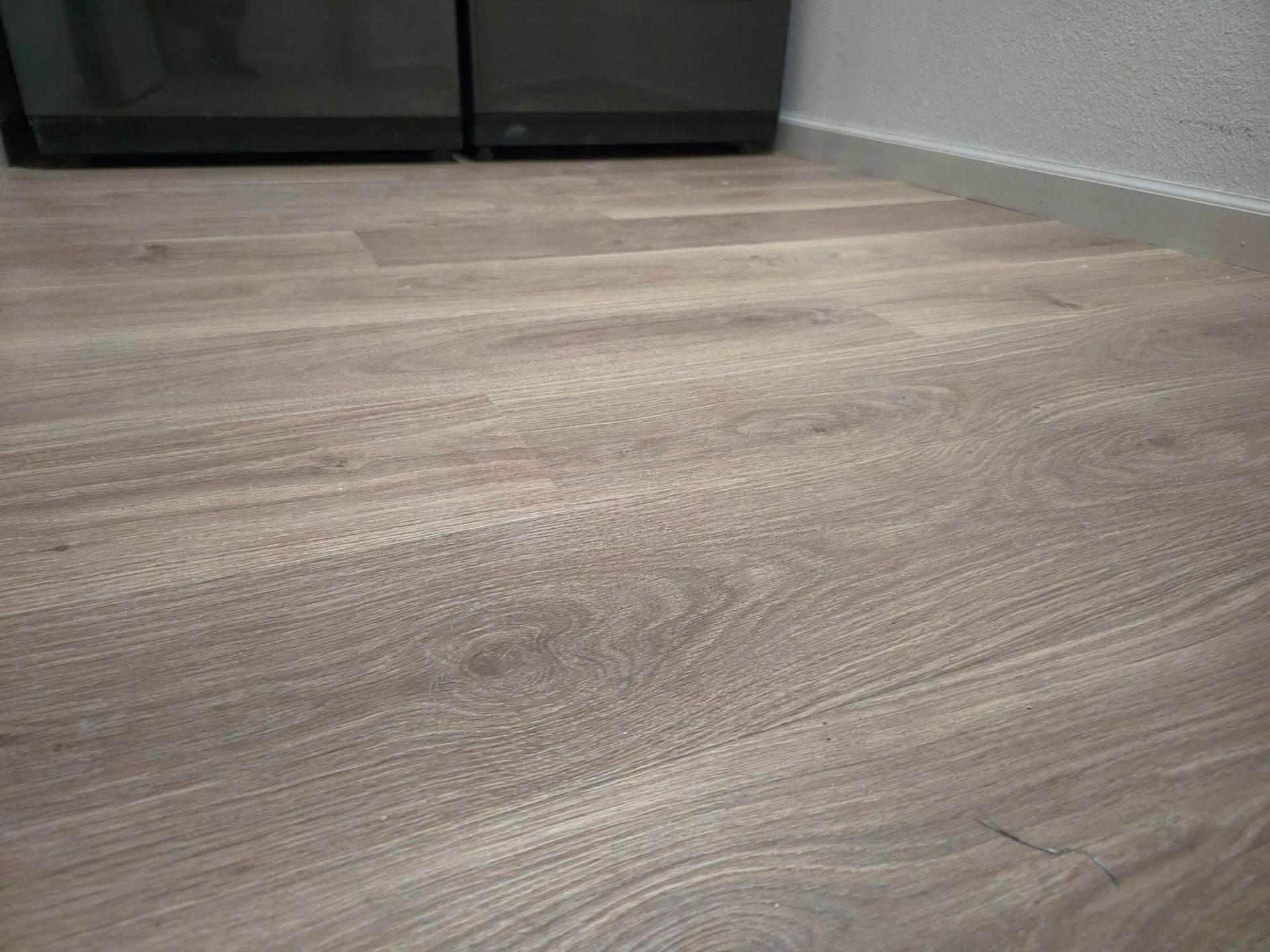 Empty room with light wood flooring and dark cabinet against a white wall