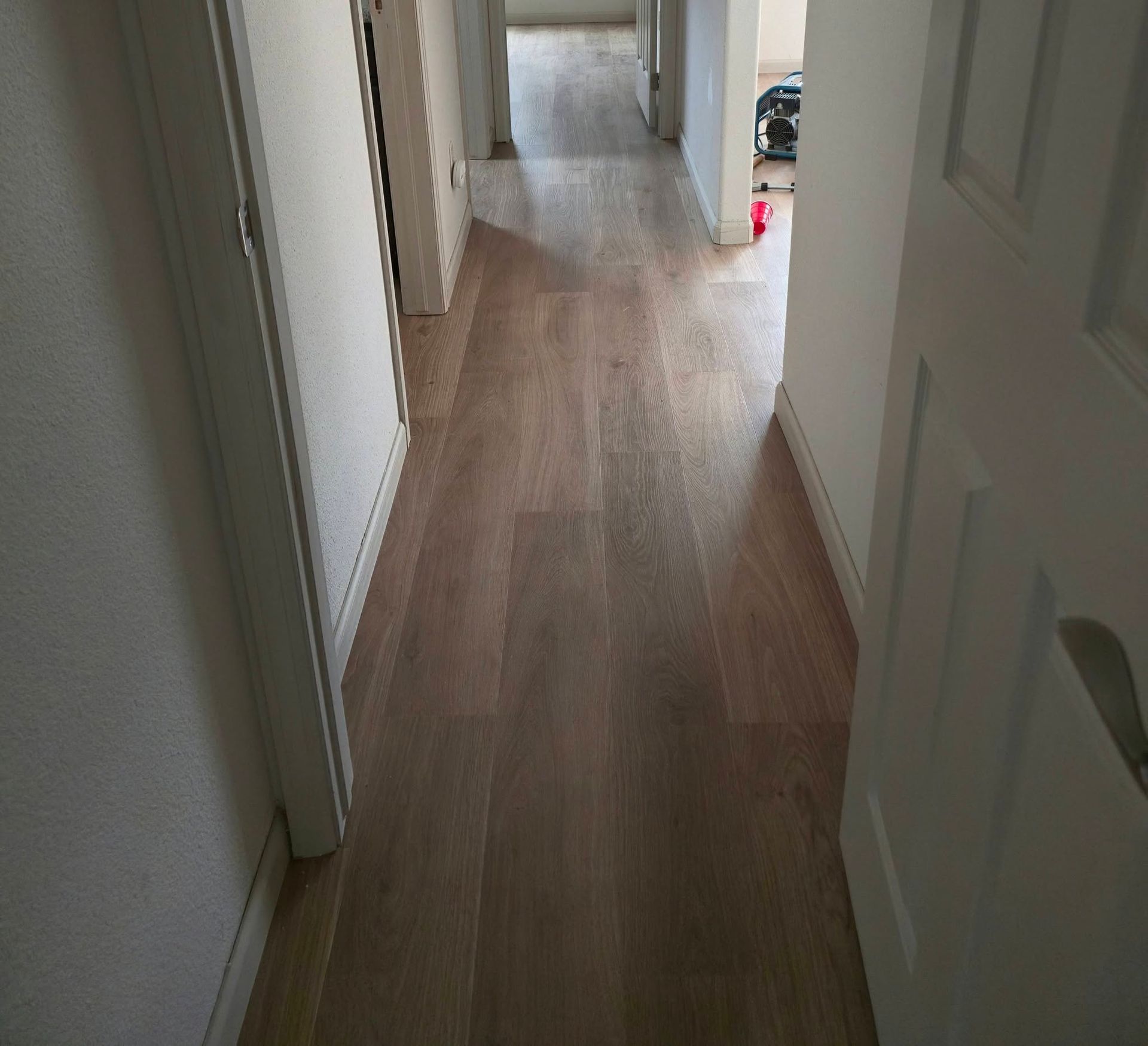 Narrow hallway with light wood flooring and white walls, viewed from an open doorway