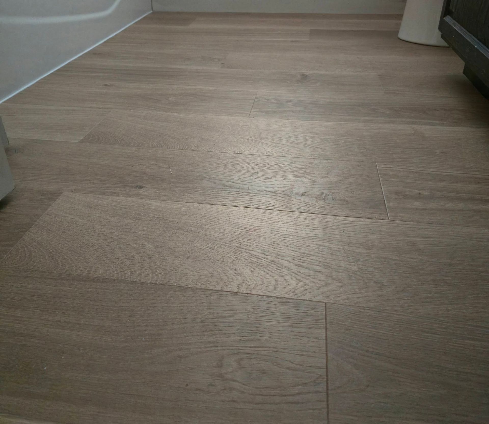 Light wood floor in a room with a white wall and a sofa edge visible on the right.