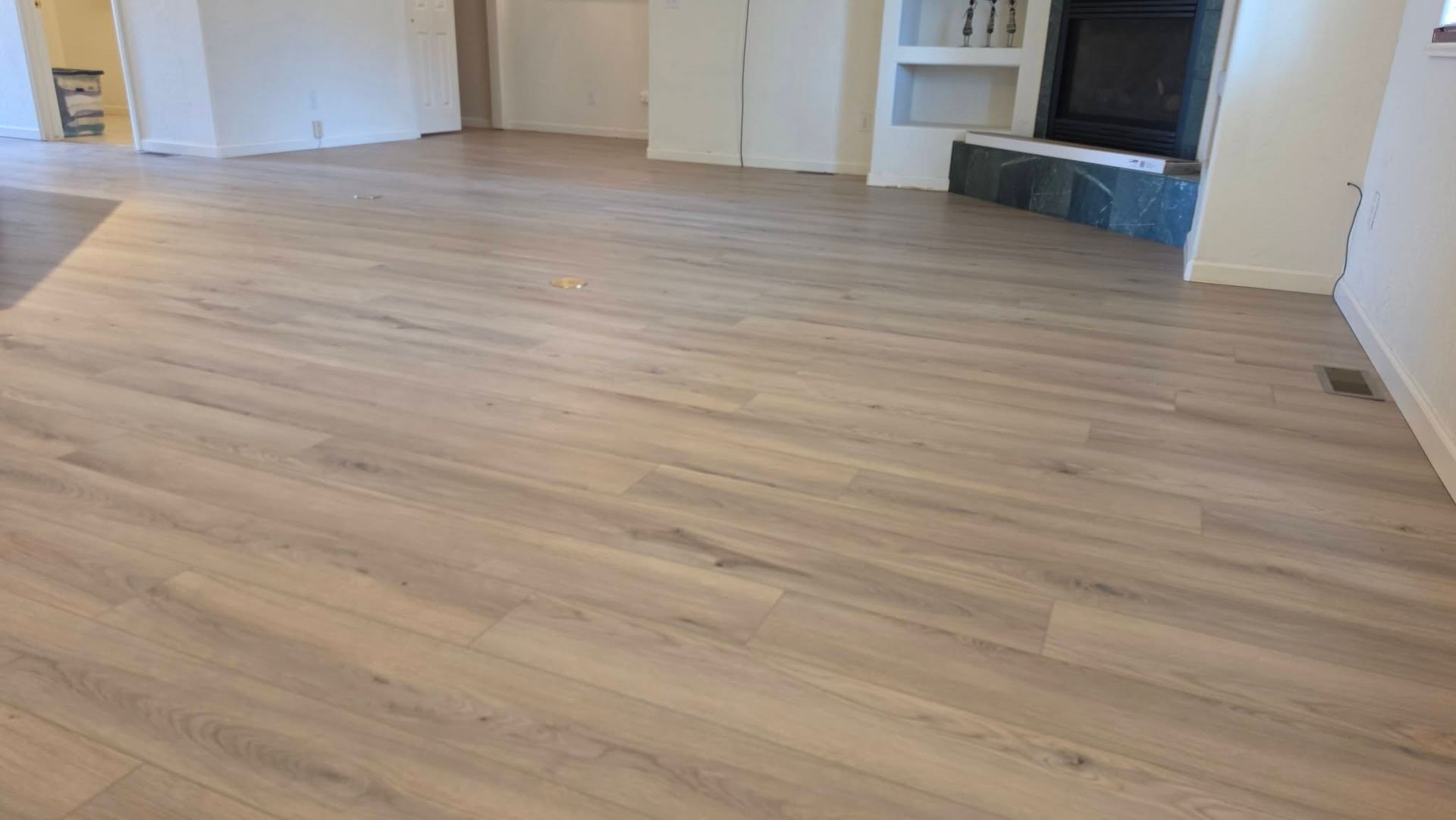 Empty room with light wood flooring and white walls, viewed from a low angle.