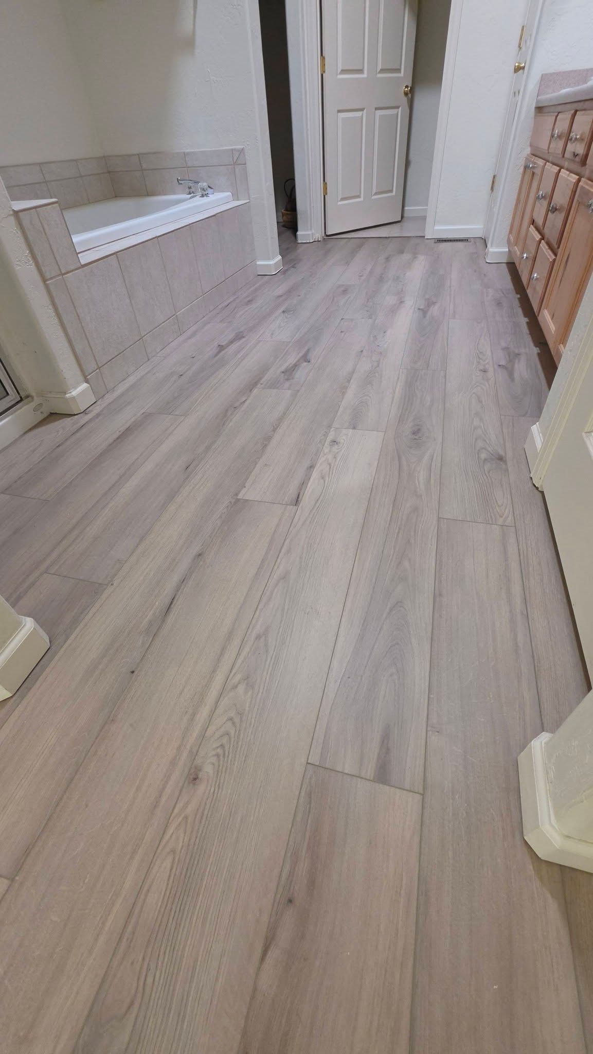 Narrow hallway with light wood flooring, white walls, and cabinets on the right.