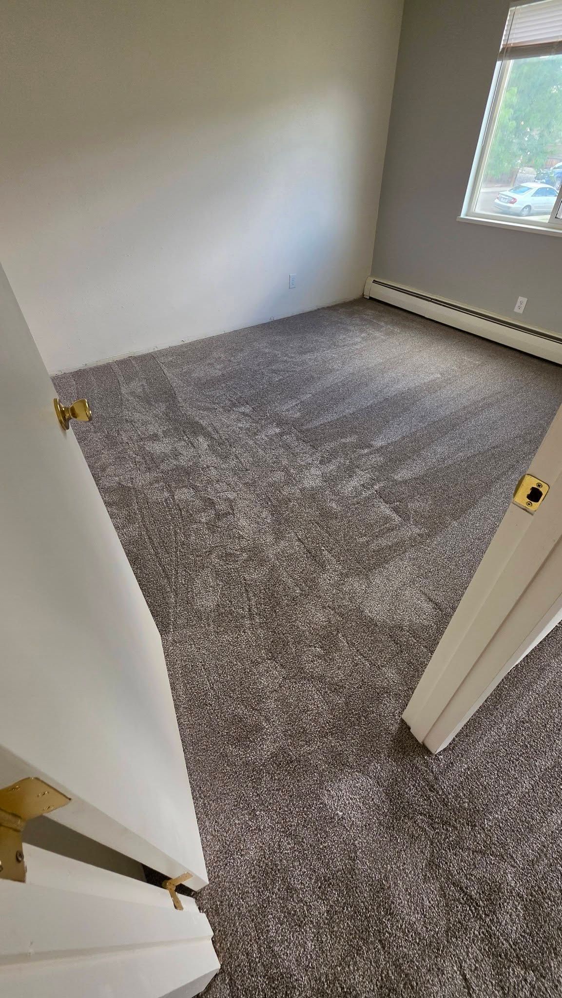 Empty bedroom with gray carpet, white walls, and a window with blinds.