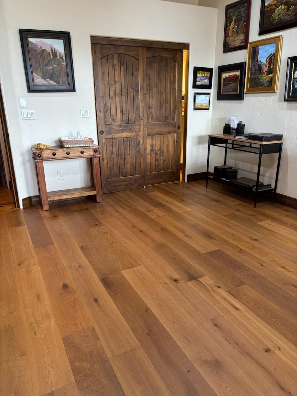Wood-floored living room with rustic double doors, framed wall art, and a small black console table.