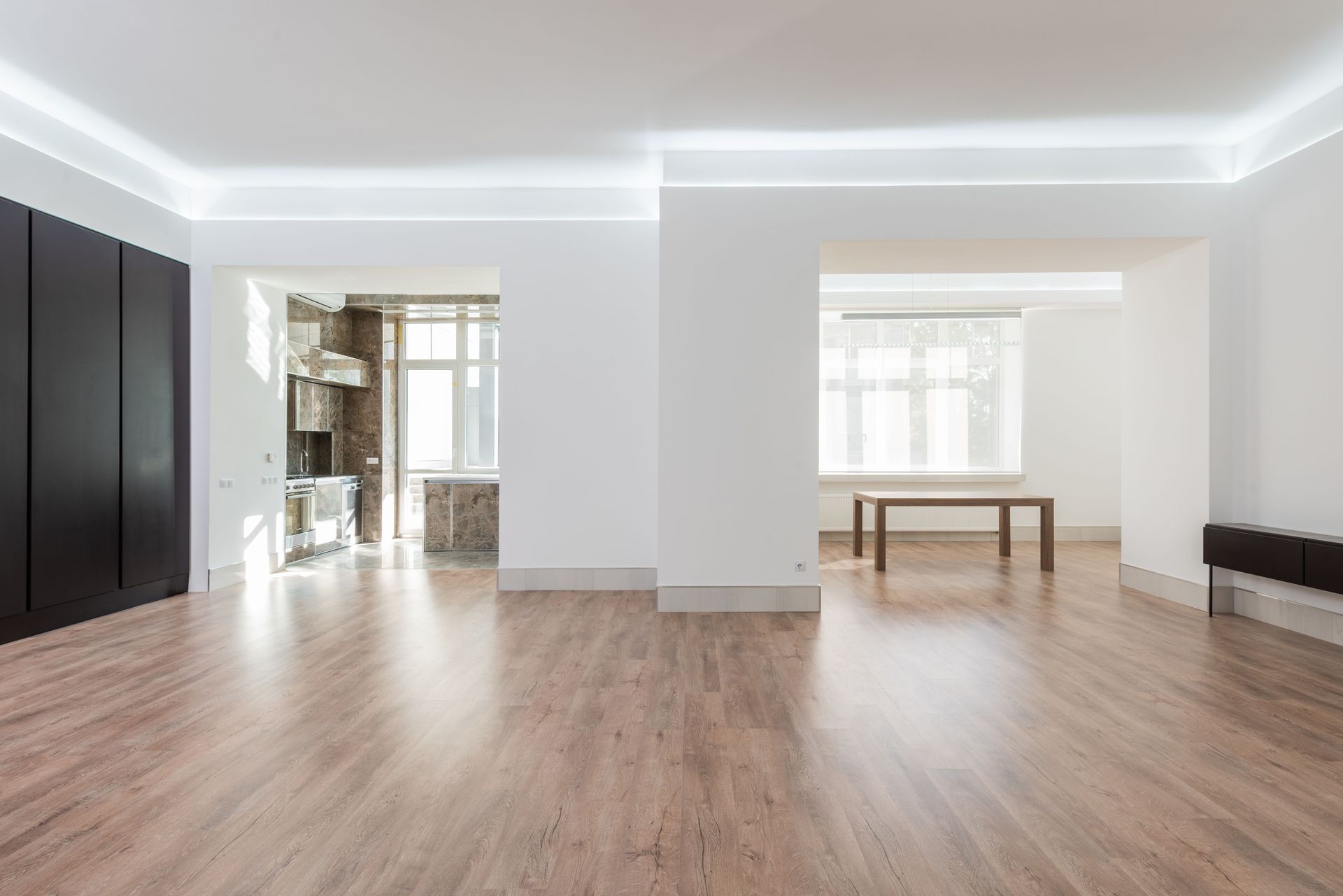 Empty modern living room with wood floors, white walls, and large windows