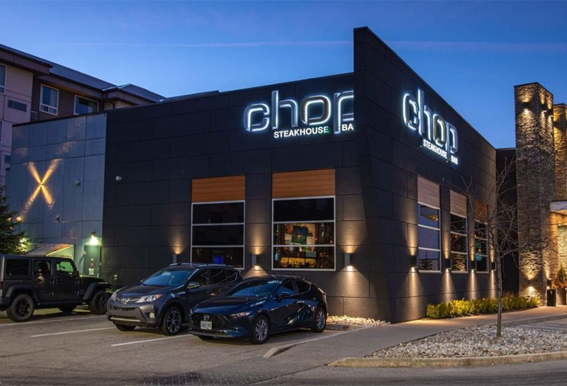 A restaurant with cars parked in front of it at night.