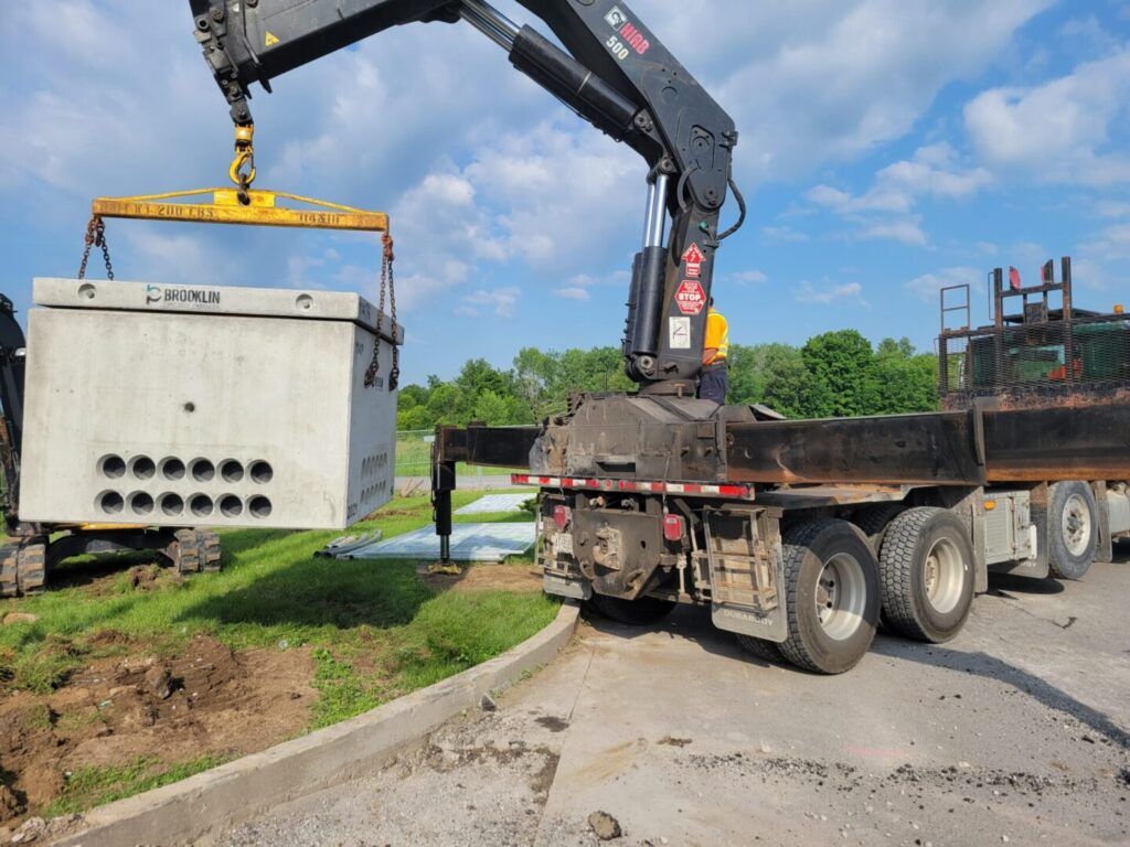 A crane is lifting a concrete box on top of a truck.