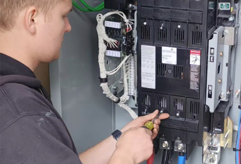 A man is working on an electrical box with a screwdriver.