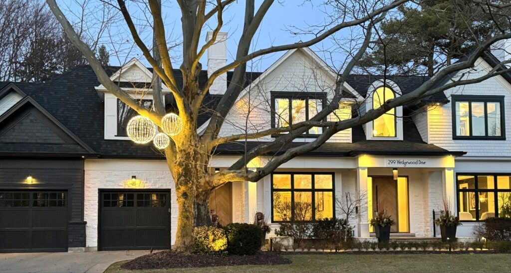 A large white house with a black garage door and a tree in front of it.
