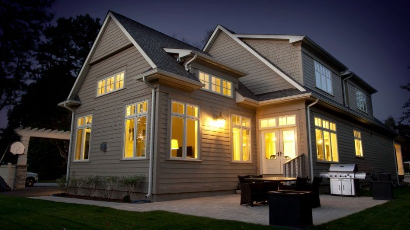 The house is lit up at night and has a grill in the backyard.