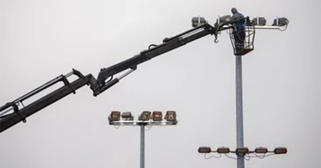 A man is working on a light pole with a crane.