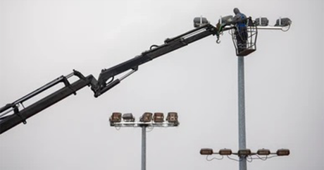 A man is working on a light pole with a crane.