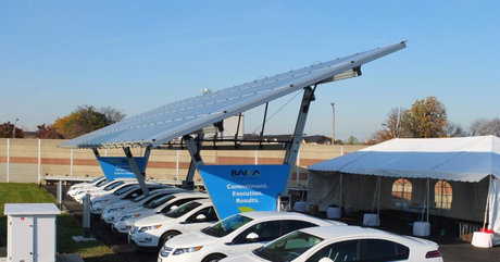 A row of cars are parked under a solar panel