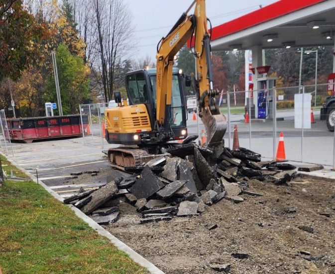 An excavator is working on a road in front of a gas station