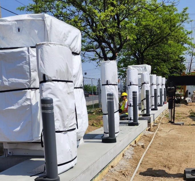 A man in a yellow hard hat stands in front of a row of white bags