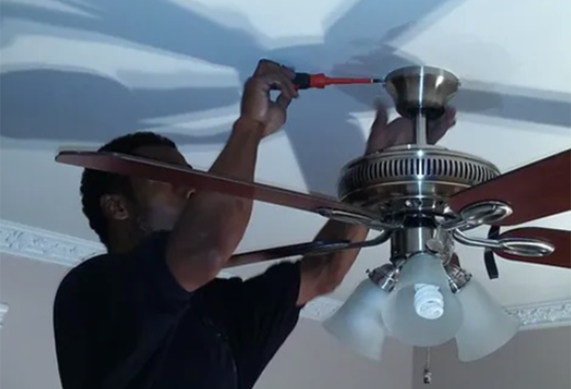 A man is fixing a ceiling fan with a screwdriver