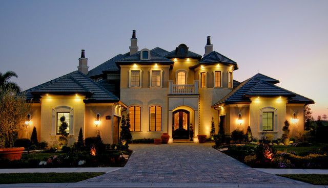 A large house is lit up at night and has a driveway leading to it